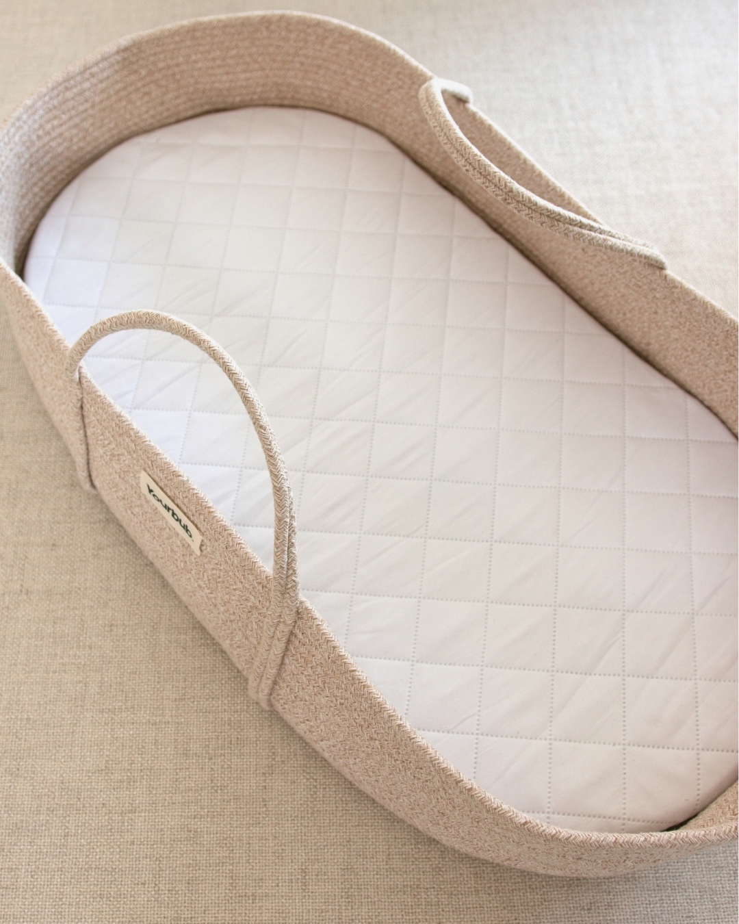 Close-up of a beige infant moses basket with a white cushion inside